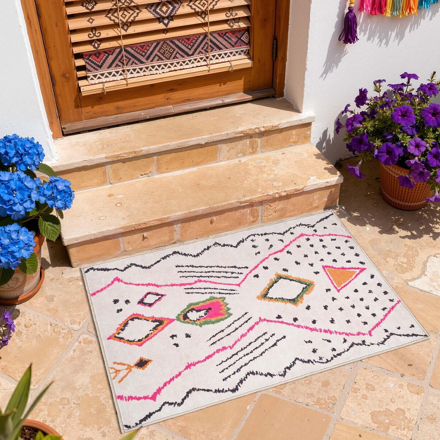 Colorful geometric patterned doormat on stone porch with blue and purple potted flowers