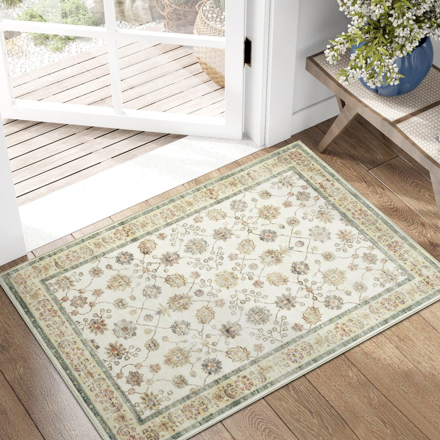 Floral patterned area rug with green and beige borders on wooden floor near glass door and side table with blue vase flowers