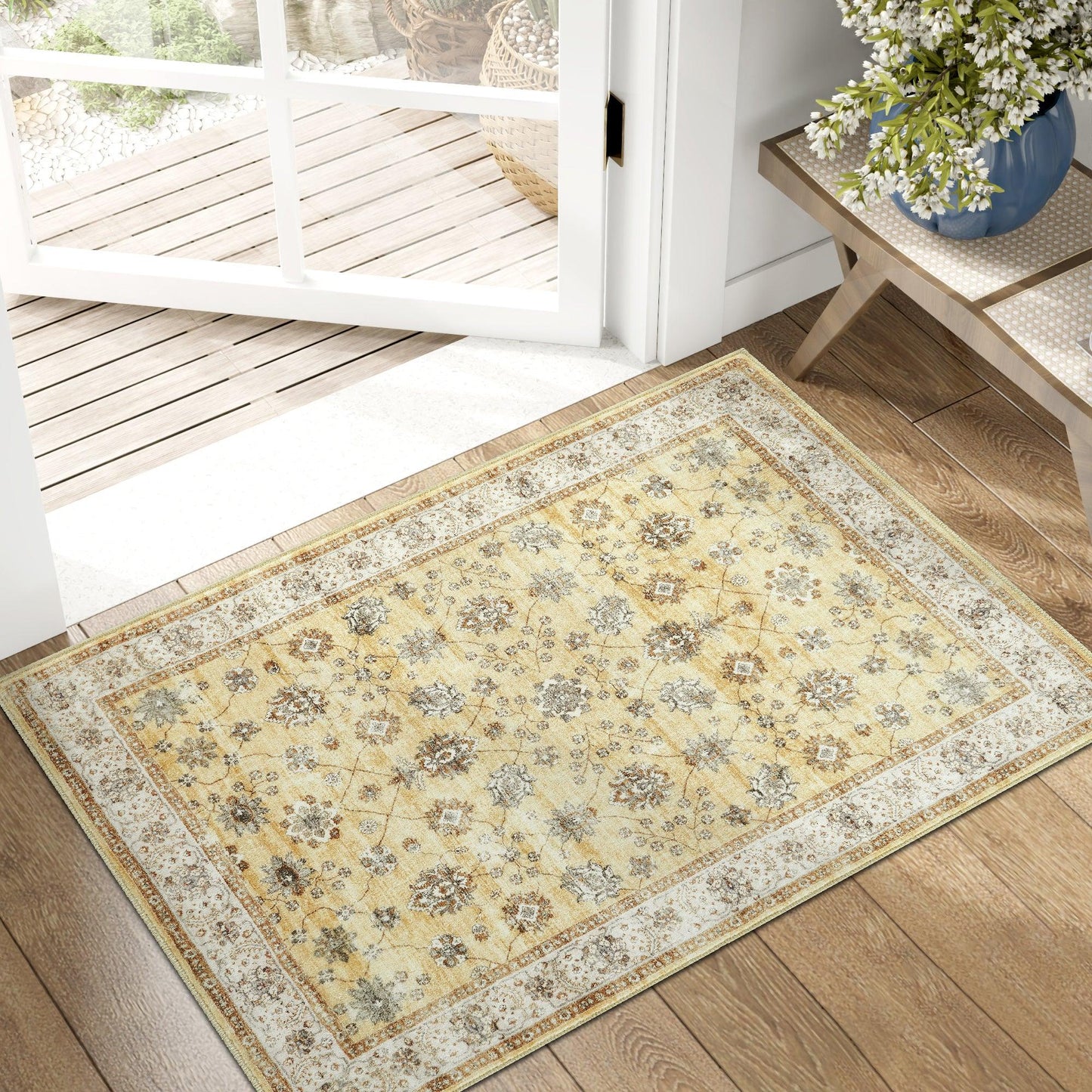 Yellow floral patterned area rug on wooden floor near open glass door and table with blue vase and white flowers
