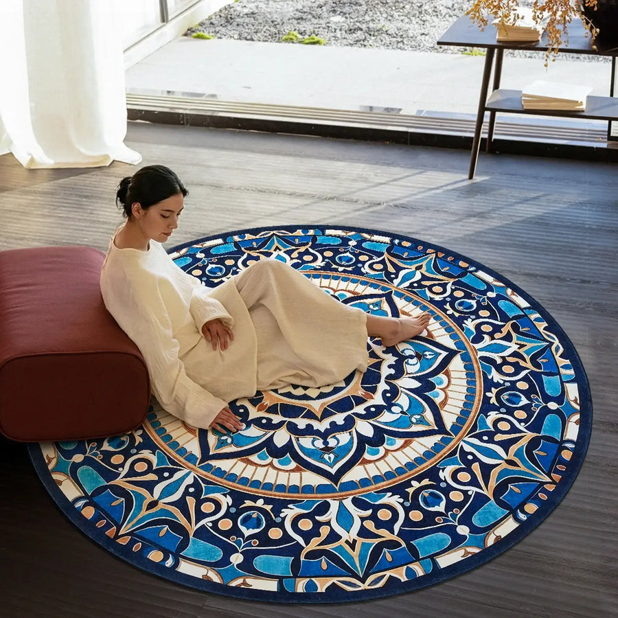 Woman in cream outfit sitting on a round blue patterned rug in modern room with dark flooring